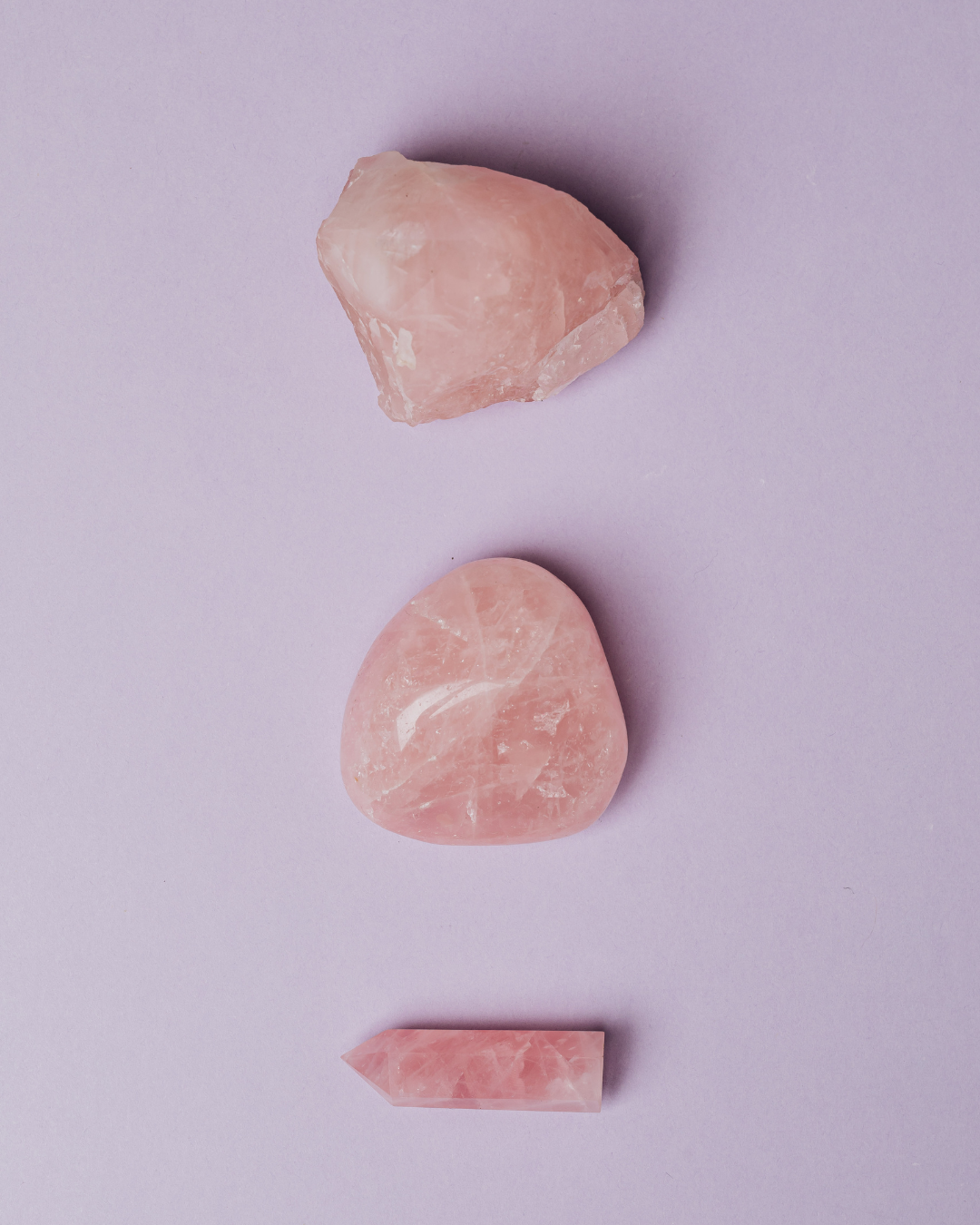 Three various shaped rose quartz stones on a lavender background for Rose Quartz benefits guide