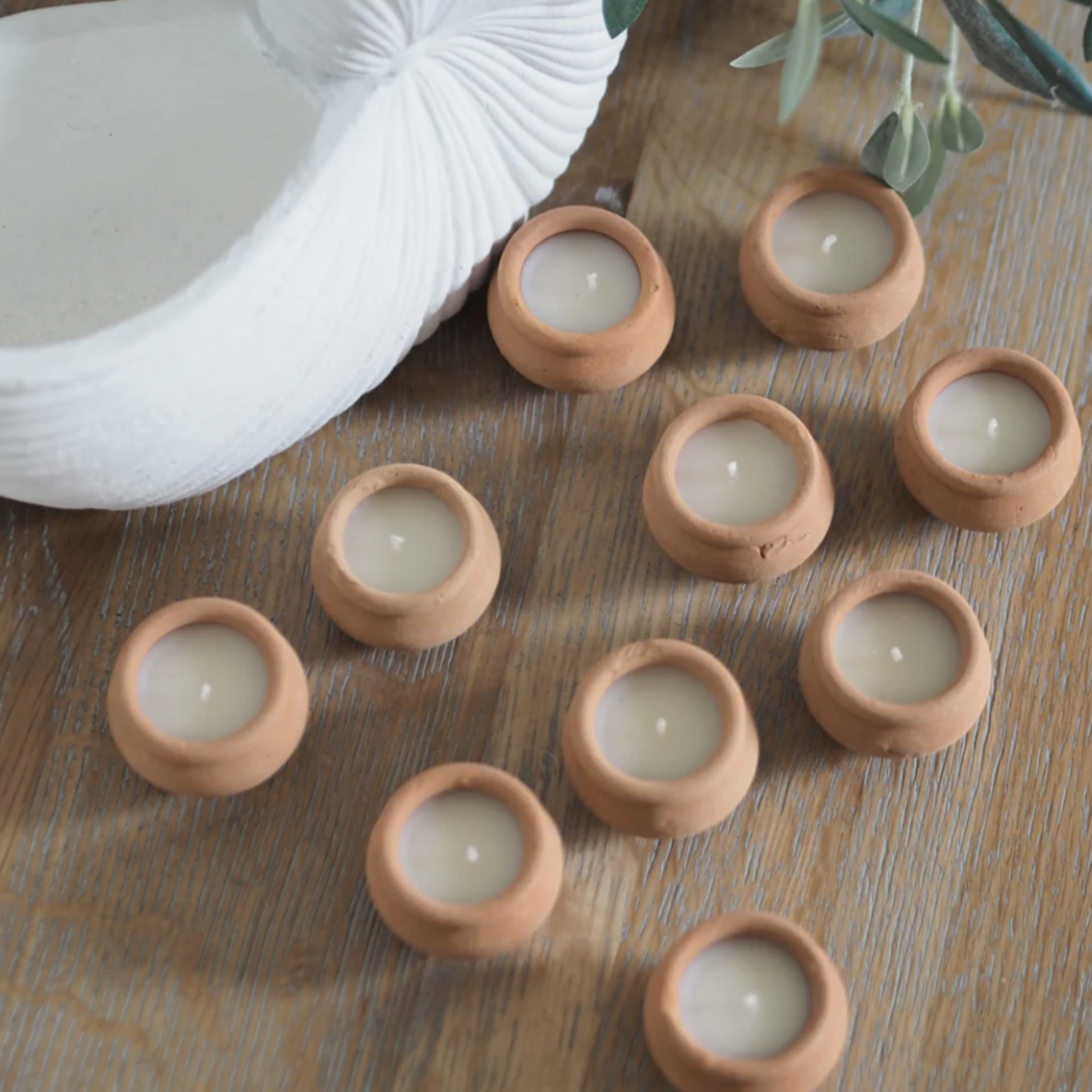 Small terracotta candles on a wooden surface with a white woven basket and greenery.