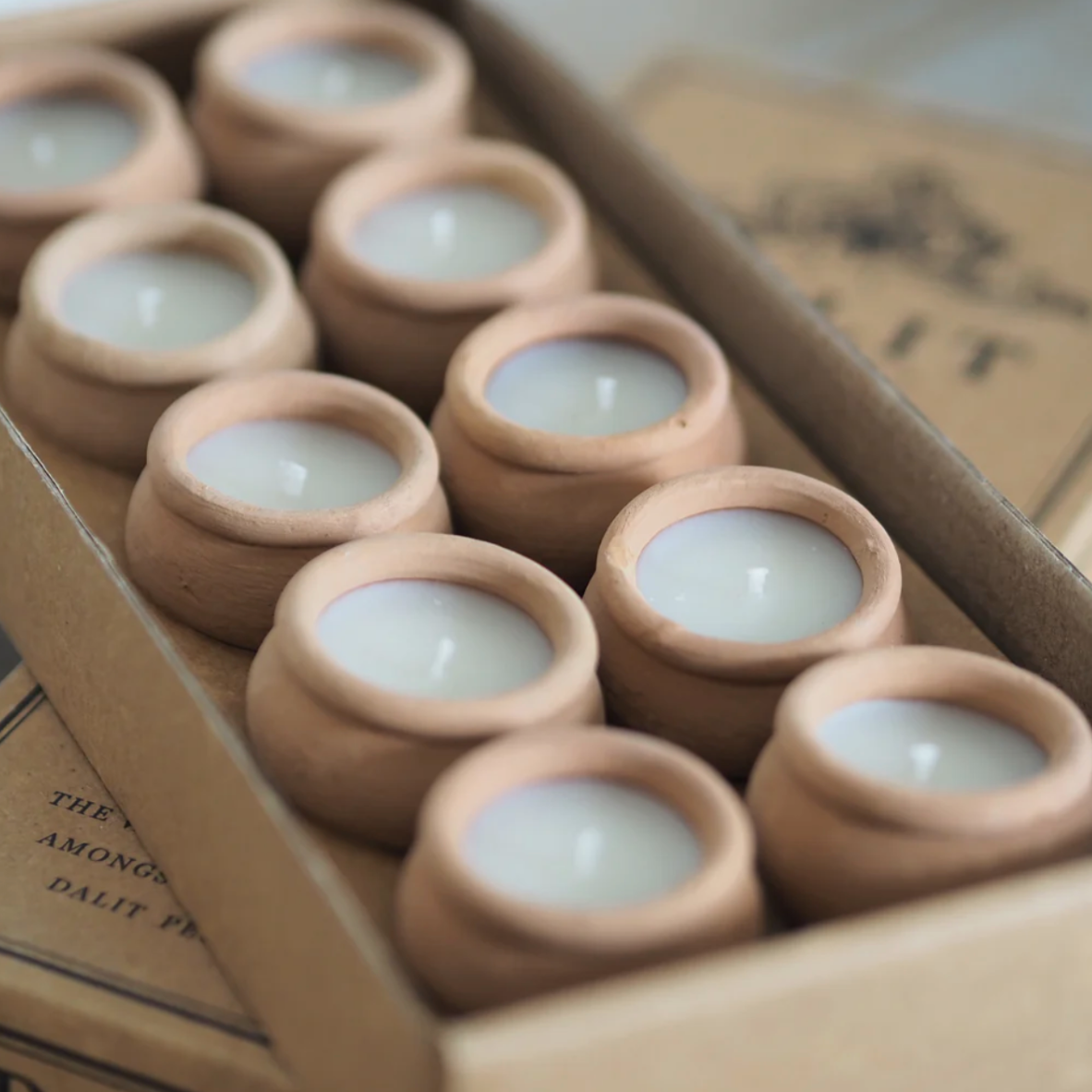 Set of small candles in terracotta holders inside a cardboard box.