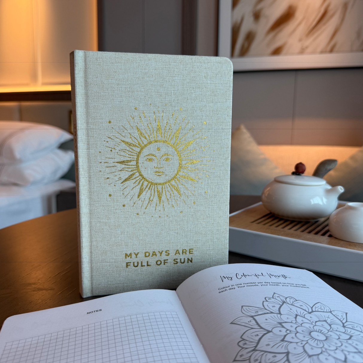 Journal with sun design and text on a table with a tea set in the background