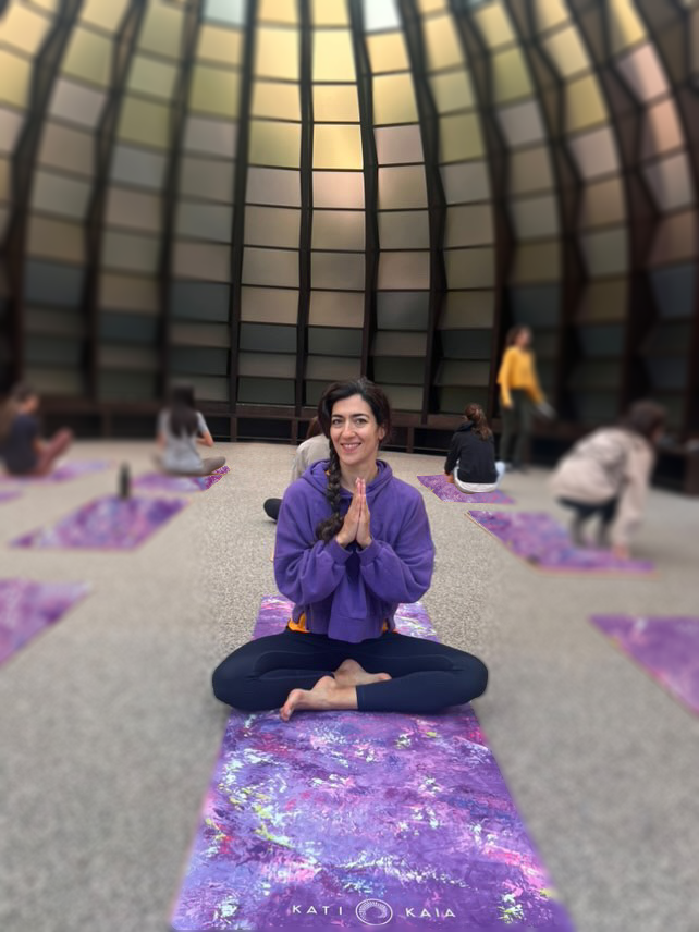 Woman in a purple sweatshirt sitting on a Kati Kaia Yoga Mat in Serpentine.