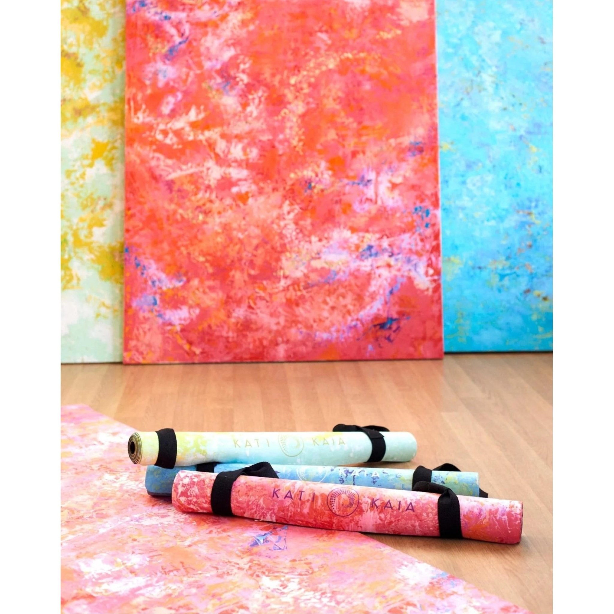 Kati Kaia artist yoga mats rolled up on wooden floor with vibrant abstract designs in red, blue, and yellow