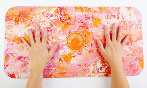 Kati Kaia Erytheia yoga pad with vibrant pink and orange abstract design and hands placed on mat