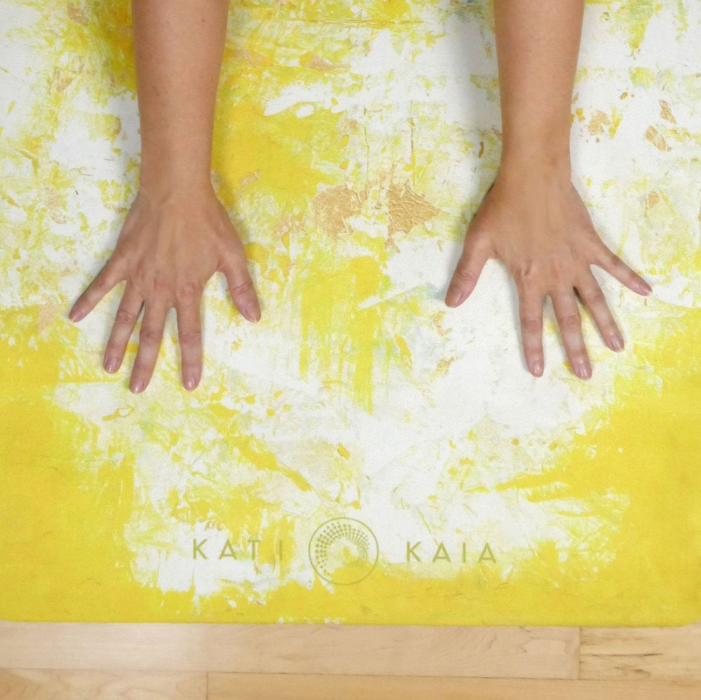Yellow artist yoga mat by Kati Kaia with abstract white and beige paint design and hands placed on mat