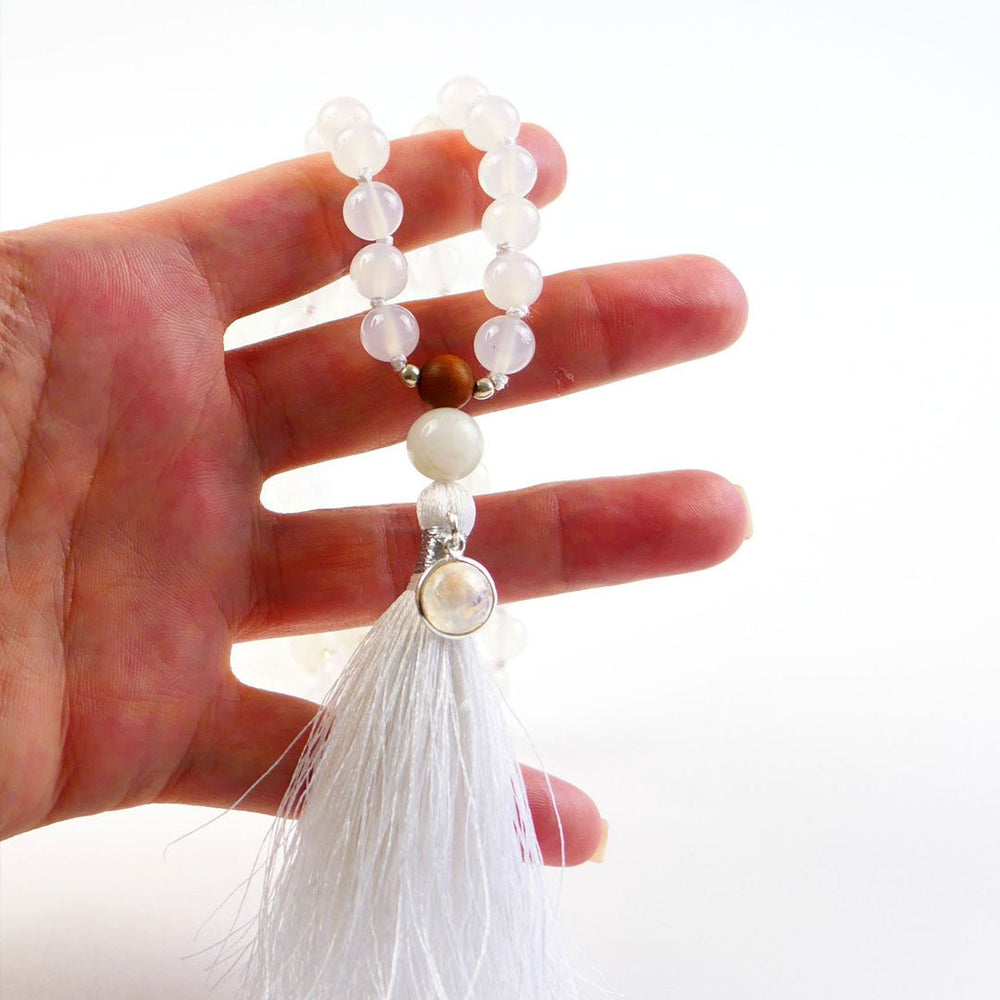 Hand holding Kati Kaia crystal moonstone mala necklace with white beads and tassel on white background