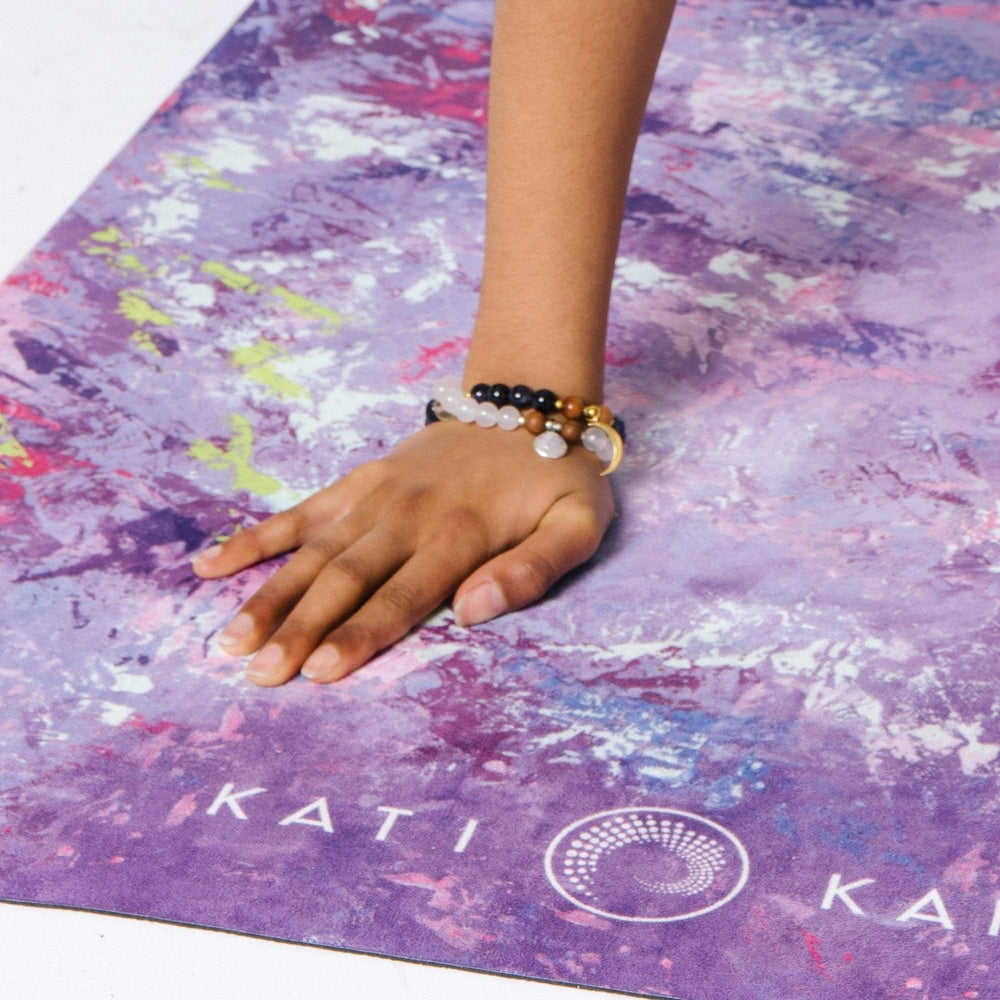 Hand wearing moonstone mala necklace set on purple Kati Kaia yoga mat with artistic design