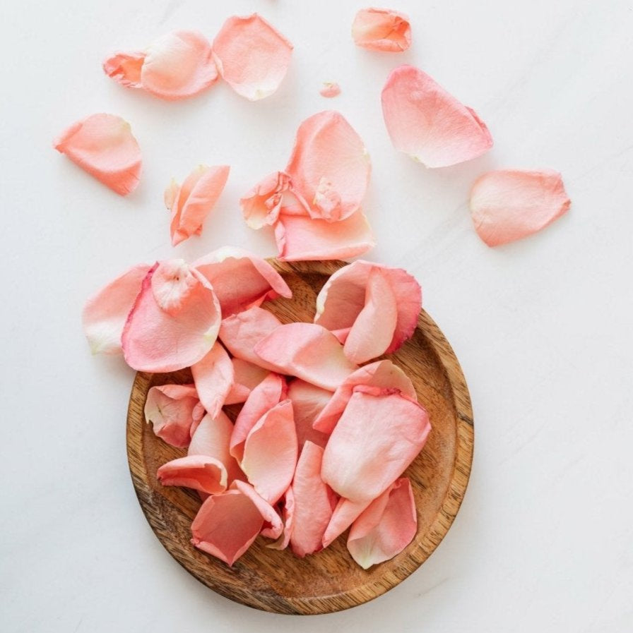 Natural pink rose petals on wooden plate symbolising Kati Kaia natural skincare tonic ingredients
