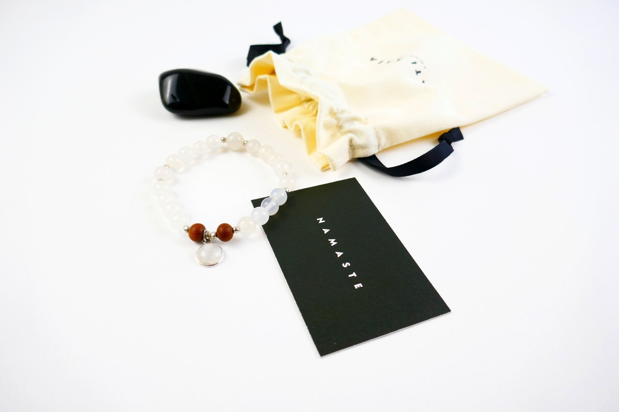 Kati Kaia Selene purity mala bracelet with white beads and brown accents beside a Namaste card and drawstring pouch